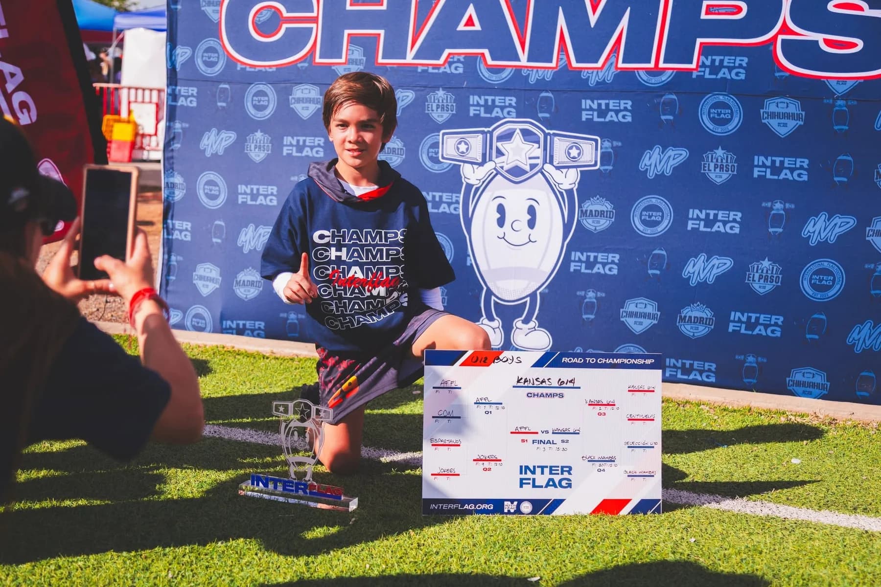 Un integrante de Kansas U12 junto al trofeo y al cuadro de competencia de Interflag